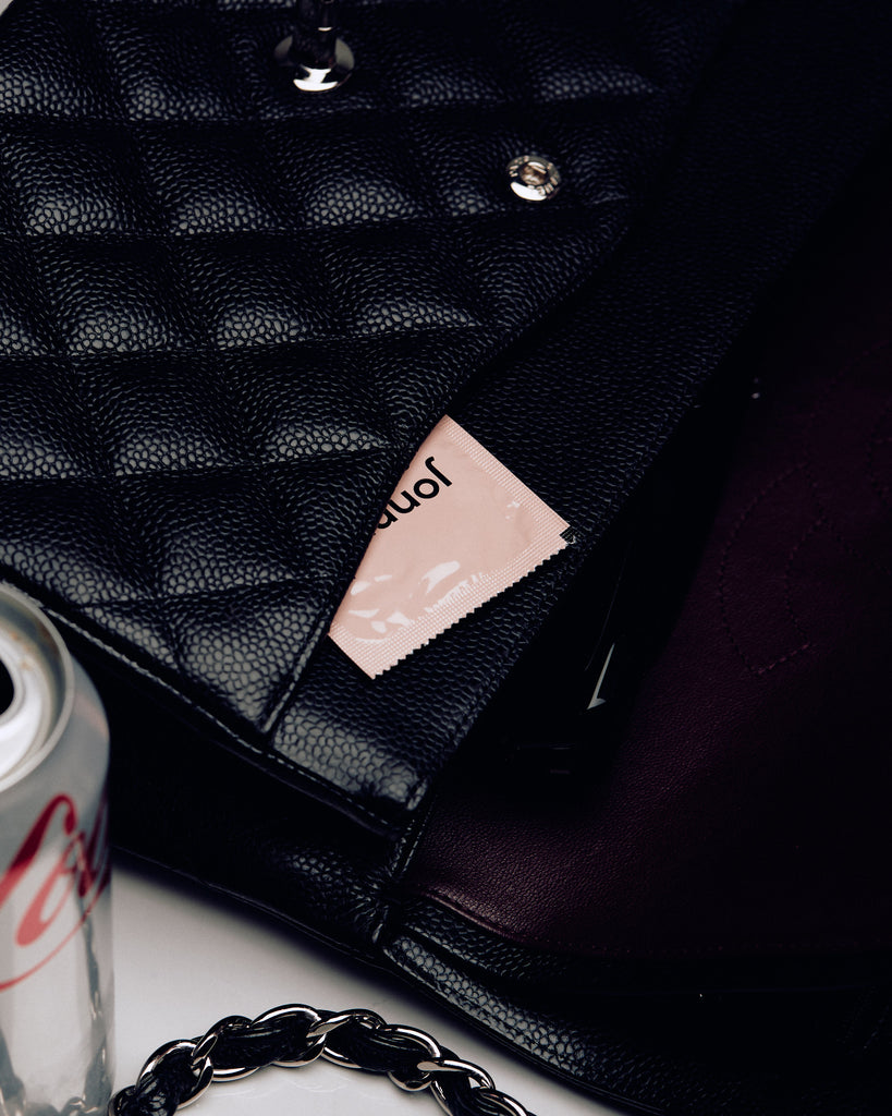 Jonny condom peeks from a chic black quilted handbag, symbolizing discreet portability and style.