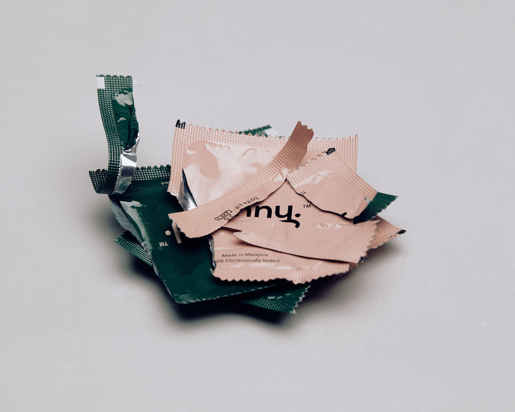 Pile of Jonny vegan condoms in green and pink wrappers, eco-friendly and tested for safety, highlighting the brand's commitment to sustainable and safe sexual health products.